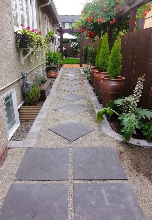 a cool and chic side yard with pavements, potted greenery and just growing greenery, bright blooms