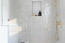 27 an elegant white shower space completely clad with white zellige tiles, with gold fixtures and a small niche for storage