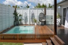 28 a cool outdoor modern space wiht a wooden deck and a plunge pool, some furniture and potted greenery and a glass fence around