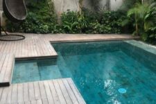 29 a cool tropical outdoor space with a wooden deck, trees and greenery around, a black woven egg-shaped chair and a plunge pool is cool