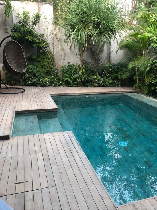 A cool tropical outdoor space with a wooden deck, trees and greenery around, a black woven egg shaped chair and a plunge pool is cool