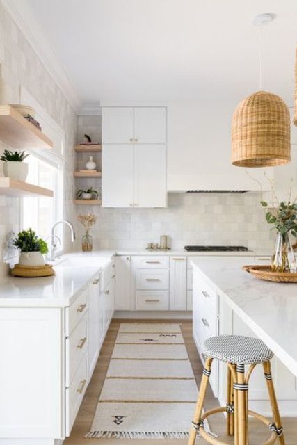 a serene white kitchen with a zellige tile backsplash, open shelves, a large kitchen island and woven pendant lamps