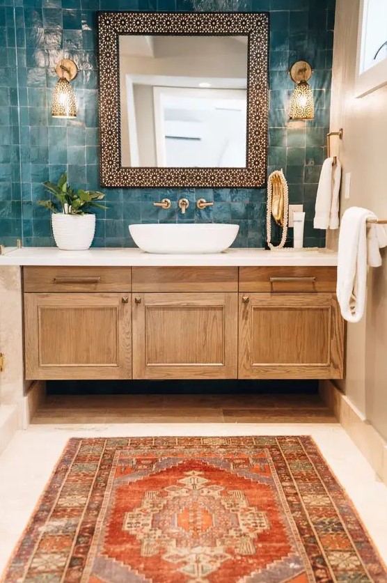 An eye catchy bathroom with a catchy teal zellige tile wall, a stained vanity, a rounded sink and a mirror in an ornated frame