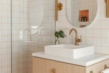 31 a bright modern bathroom with white square tiles with orange grout and orange penny tiles, a timber vanity, an oval mirror and brass fixtures