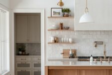31 a sophisticated neutral kitchen with white and stained cabinets, a white zellige tile backsplash, a large hood and pendant lamps