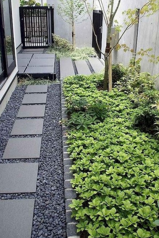 a dreamy modern side yard with pebbles and stone tiles, with flower beds with greenery and trees is a chic space with a touch of Zen