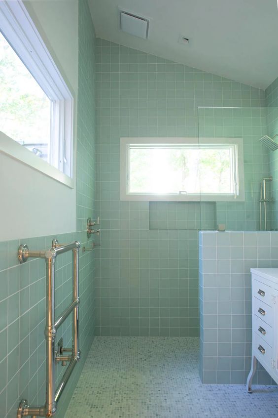 a catchy pastel green bathroom with square tiles and a shower space, a white vanity, a couple of windows to let natural light in