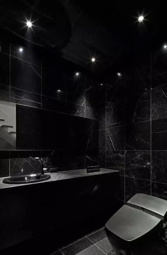 a chic black bathroom with black marble tiles and a black marble vanity plus a black toilet