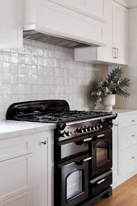 an elegant creamy kitchen with shaker cabinets and matching neutral zellige tiles, a stylish black cooker