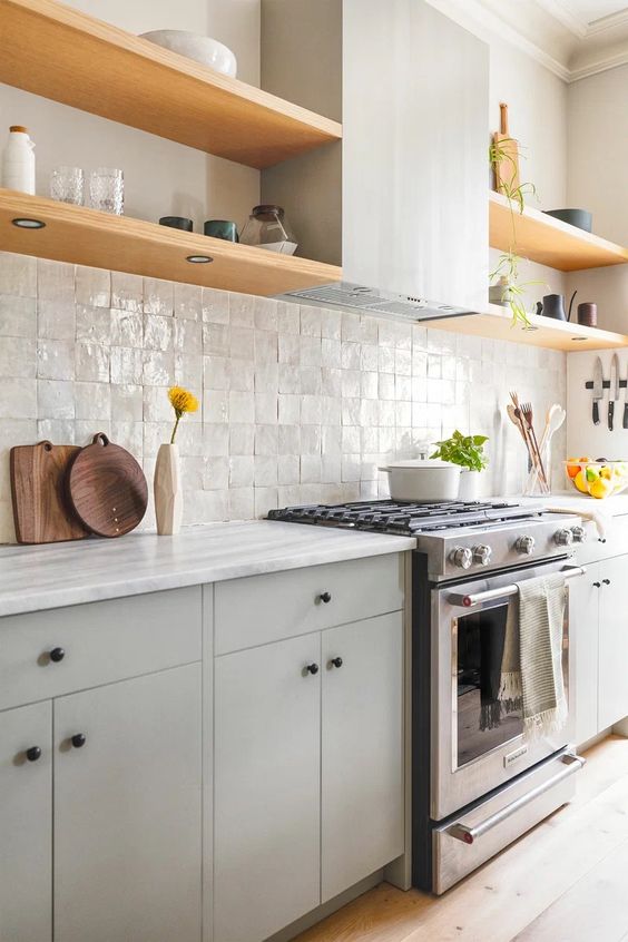 a modern grey kitchen with a zellige tile backsplash, open shelves, a hood and black knobs for a catchy detail