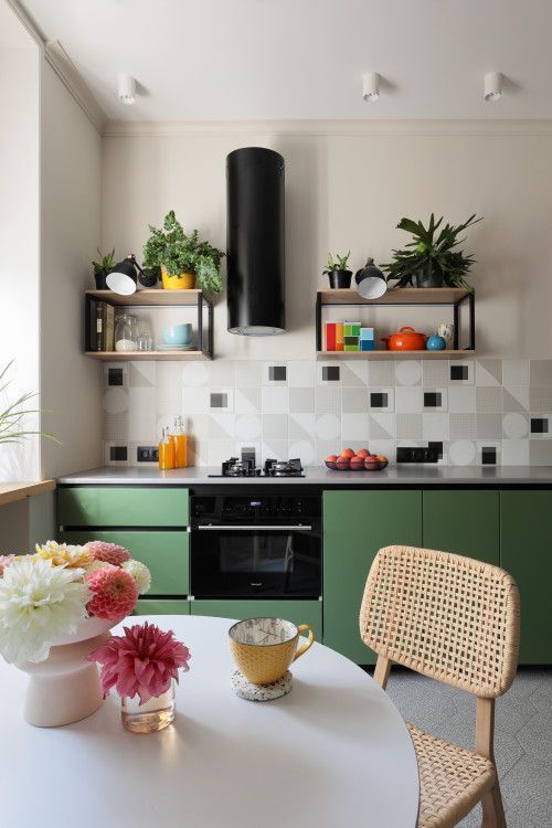a bright modern kitchen with matte green lower cabinets, square tiles with a geo print, a black hood and some shelves