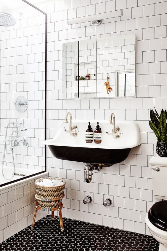 a contrasting modenr bathroom with white square tiles and hex tiles on the floor, a black wall-mounted sink, a mirror and some potted plants