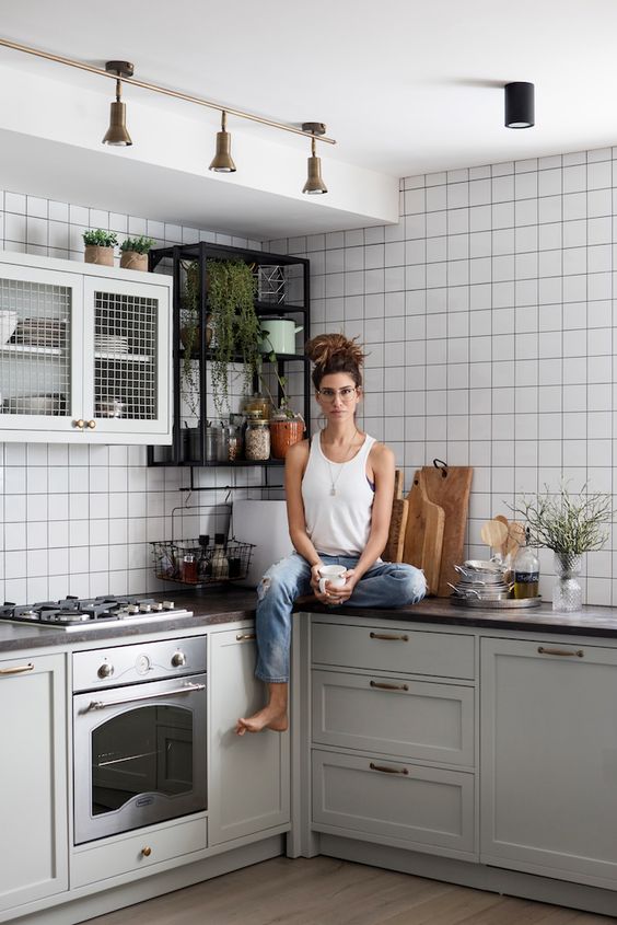 a chic grey kitchen with shaker cabinets, a white square tile backsplash, small upper cabinets and a shelf