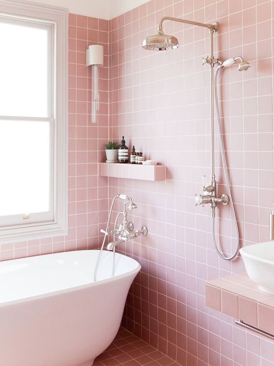a lovely pink bathroom with square tiles, a little shelf and a tiled vanity, white appliances and stainless steel fixtures