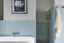 41 a modern bathroom with neutral walls and light blue square tiles, an oval tub and some artwork is amazing