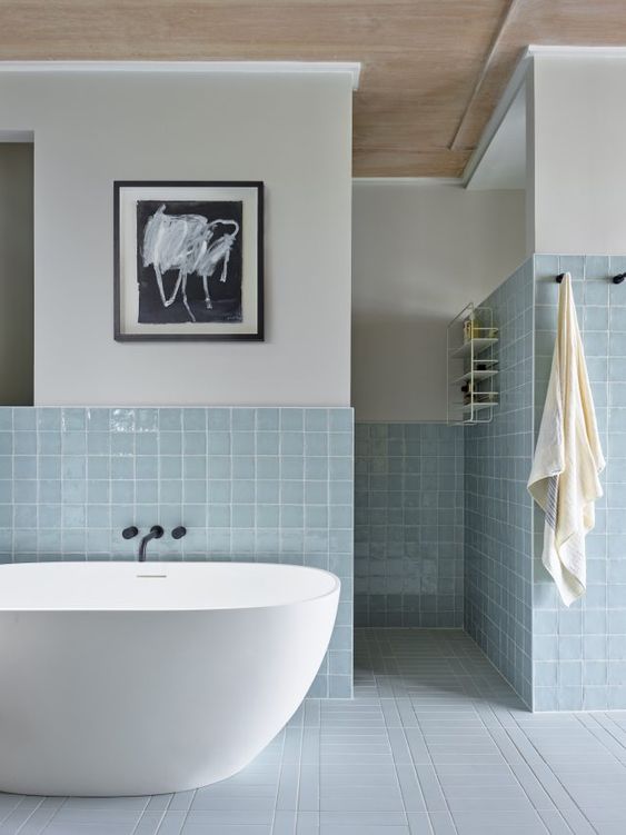 a modern bathroom with neutral walls and light blue square tiles, an oval tub and some artwork is amazing