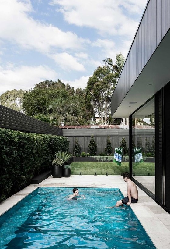 a modern outdoor space with a greenery zone, a living wall, a pool with a stone deck and a glass fence is a lovely nook