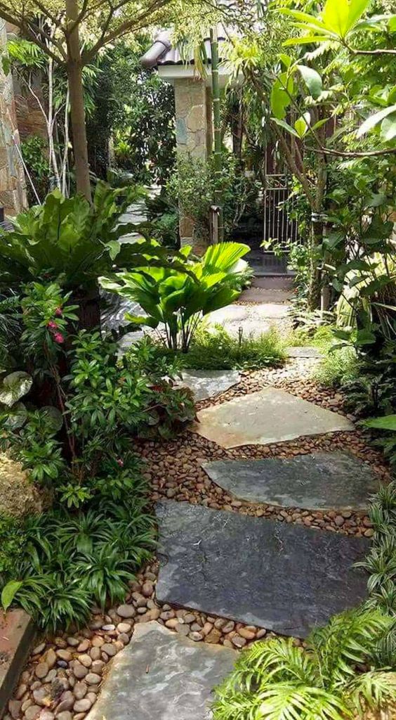 a lush side yard with pebbles, irregular stones, lots of greenery and blooms and some trees around