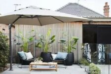 43 a pretty tropical backyard with a blue pool, a parasol, potted plants and a coffee table, greenery and a stone deck