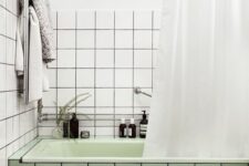44 a modern bathroom with square white and green tiles, a light green tub, some neutral textiles and decor