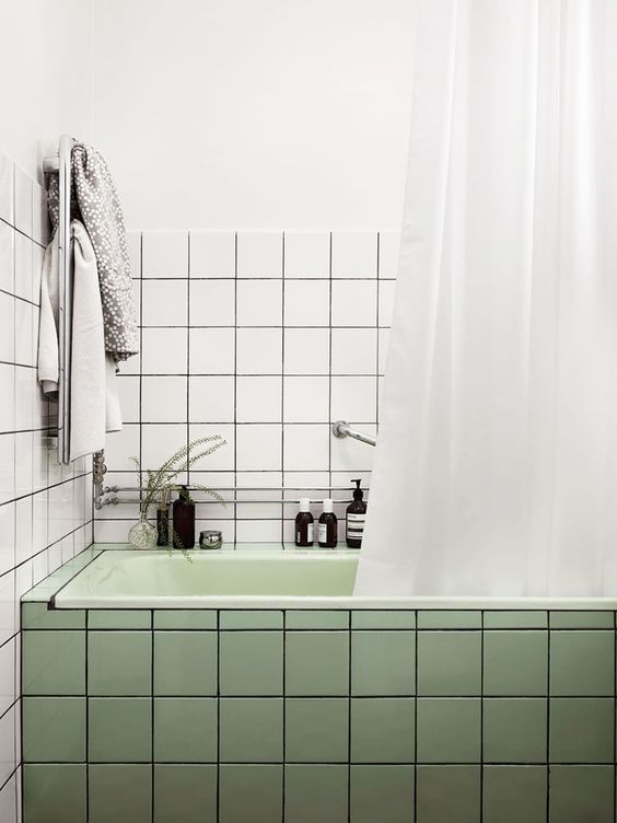 a modern bathroom with square white and green tiles, a light green tub, some neutral textiles and decor