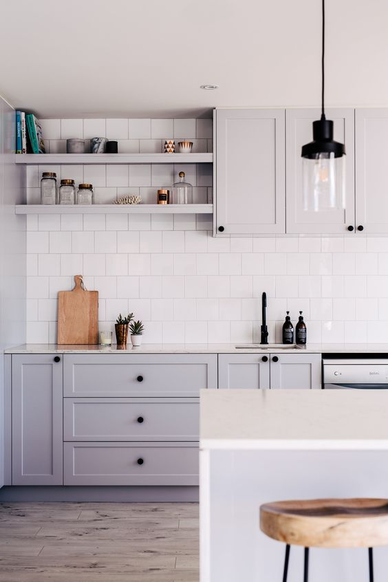 a grey Scandinavian kitchen with shaker cabinets, white stone countertops, white square tiles on the backsplash and pendant lamps
