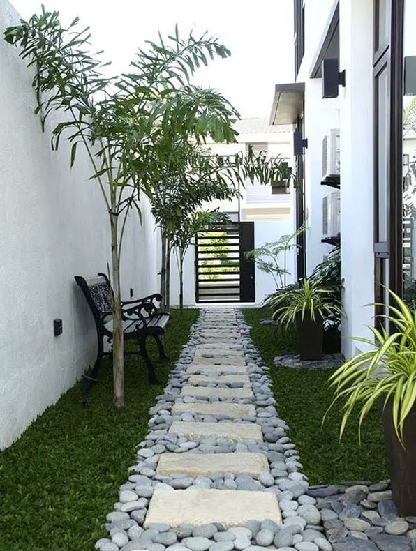a modern and minimal side yard with a green lawn, pebbles and stone pavements, potted plants and some small trees
