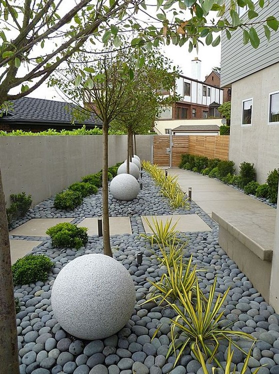 a modern side yard styled with tiles and grey pebbles, stone balls, trees, greenery and succulents is a stylish space that catches an eye