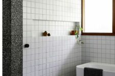 47 a modern bathroom with white square tiles, a grey terrazzo floor, a tub and a shower space, black fixtures