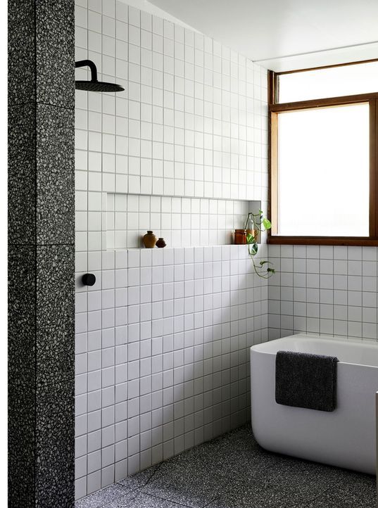 a modern bathroom with white square tiles, a grey terrazzo floor, a tub and a shower space, black fixtures