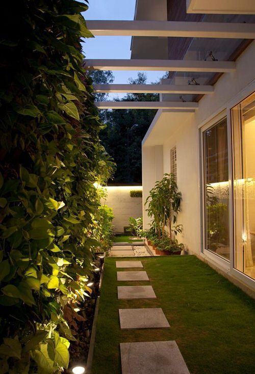 a modern side yard with a green lawn, pavements, a living wall and additional built-in lights to make it more welcoming