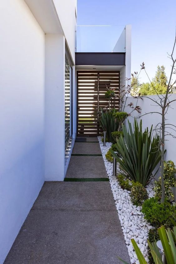 a modern side yard with pavements, white pebbles, greenery and shrubs and some trees is a cool and stylish space