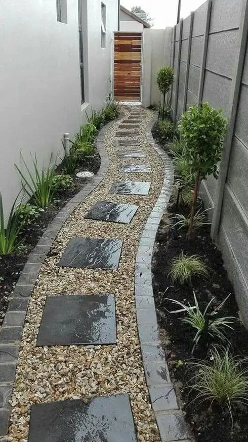 a narrow side yard styled with pebbles and stone pavements, greenery and little trees is a lovely and elegant space