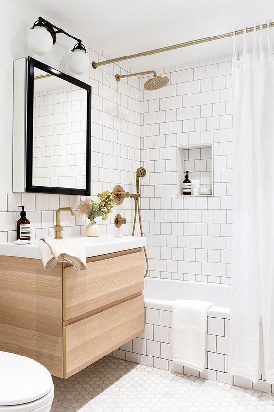 a neutral bathroom clad with white square tiles and hexagon ones, a tub clad with tiles, a timber vanity and brass fixtures