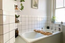 52 a neutral bathroom with a tub clad with green shiplap, white square tiles, a printed tile floor, potted plants and artwork