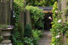 52 a refined vintage-inspired side yard with a pavement path, greenery and blooms, climbing plants and a vintage urn with blooms