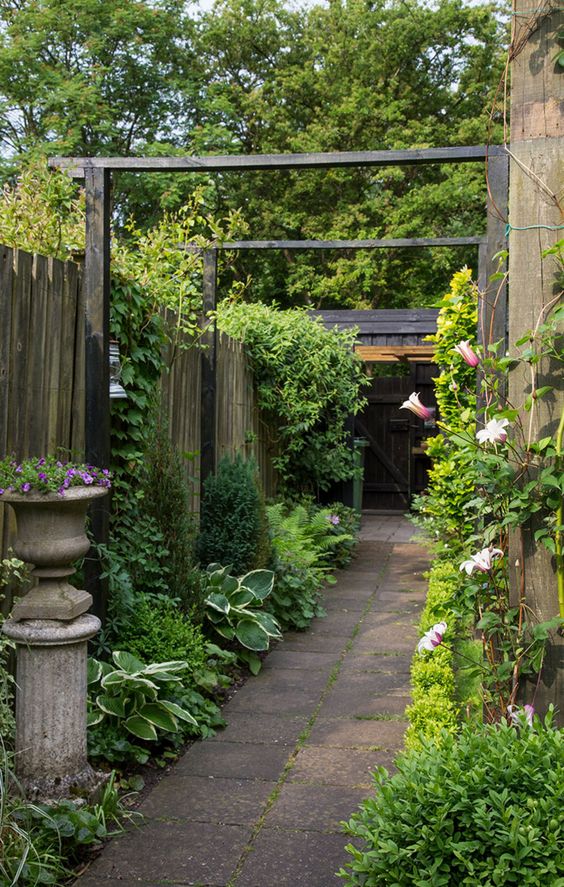 A refined vintage inspired side yard with a pavement path, greenery and blooms, climbing plants and a vintage urn with blooms