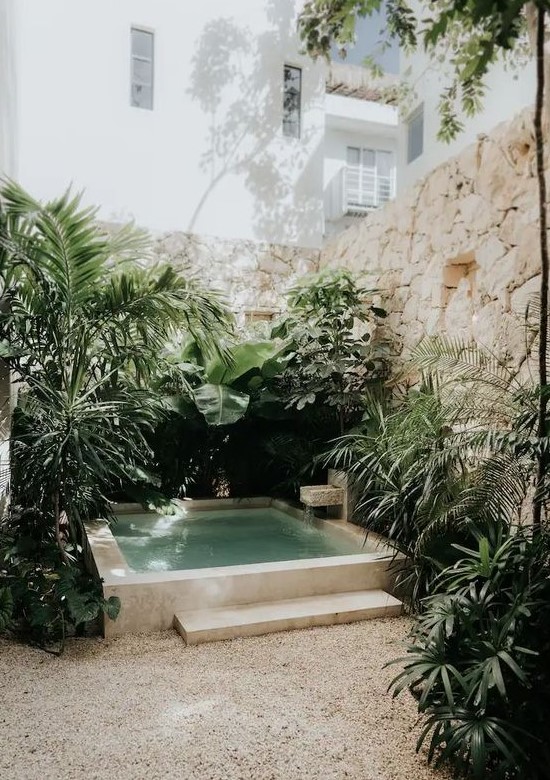 a tropical nook with stone walls, a plunge pool with a waterfall and stone borders, lots of tropical greenery around
