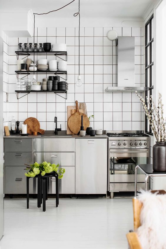 a Nordic kitchen with stainless steel cabinets and appliances, a shelving unit and a white square tile backsplash