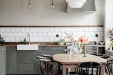 54 a Nordic kitchen with grey shaker cabinets, white square tiles, a stained table and black chairs, pendant lamps
