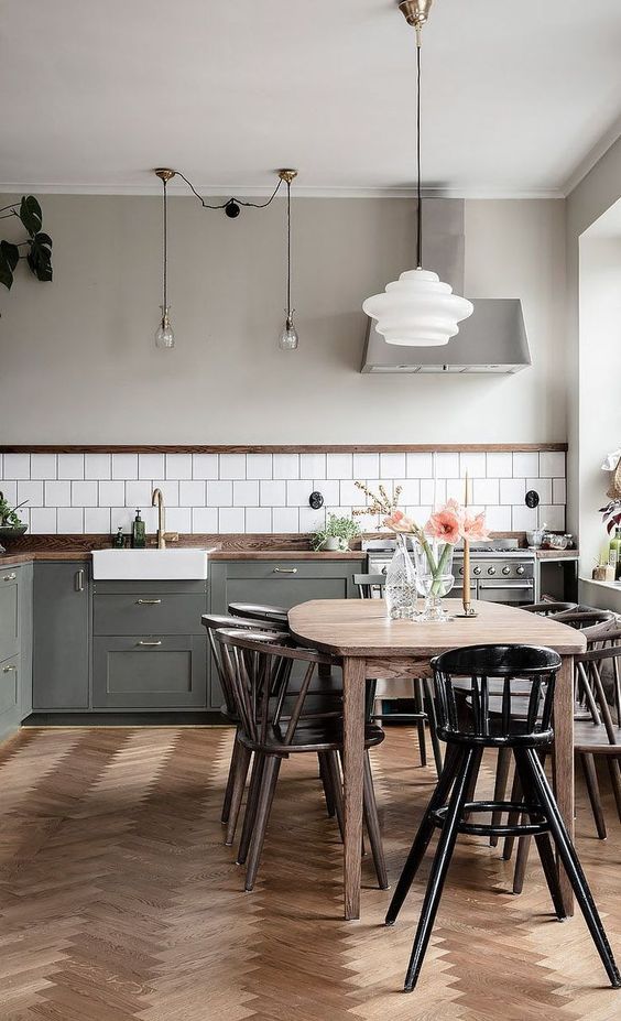 a Nordic kitchen with grey shaker cabinets, white square tiles, a stained table and black chairs, pendant lamps