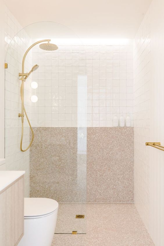 a neutral bathroom with blush terrazzo and white square tiles, a floating vanity and some brass and gold fixtures