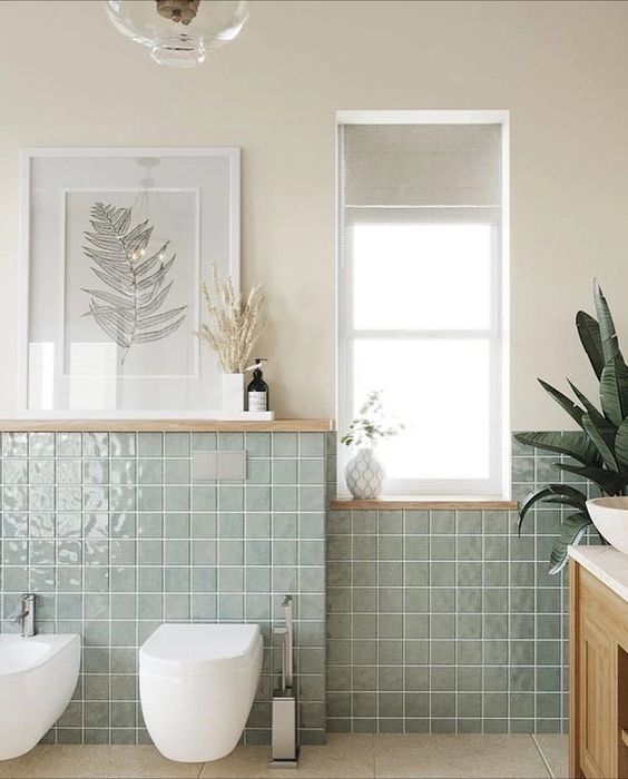a neutral bathroom with tan walls, light green square tiles, a timber vanity, some cool decor that makes it peaceful