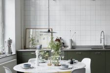 55 a pretty Nordic kitchen with dark green lower cabinets, white square tiles, a round table and white Chairs and grey lamps