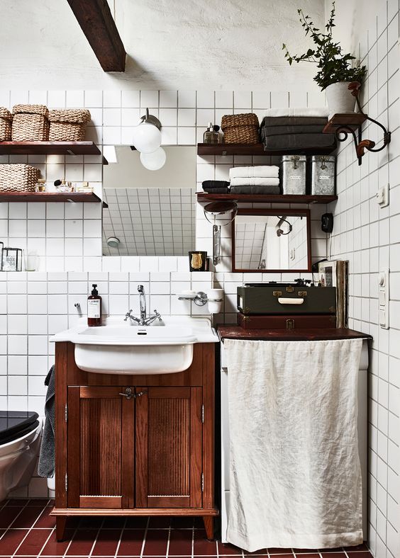 a Scandinavian bathroom with white square tiles, brown ones on the floor, a dark-stained vanity and matching shelves