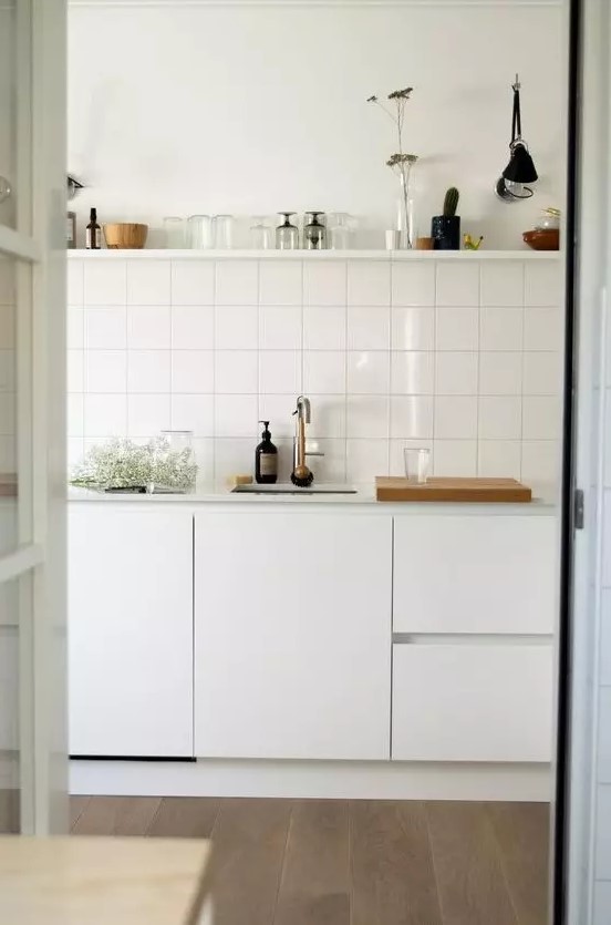 a Scandinavian kitchen in white, with a stacked square tile backsplash and an open shelf over the cabinets