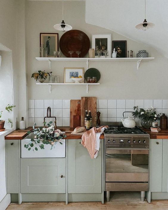 a Scandinavian kitchen with pale green shaker cabinets, butcherblock countertops, a white square tile backsplash and open shelves