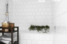 58 a simple white bathroom with white square tiles and a grey marble tile floor, a black shelving unit, some greenery and decor
