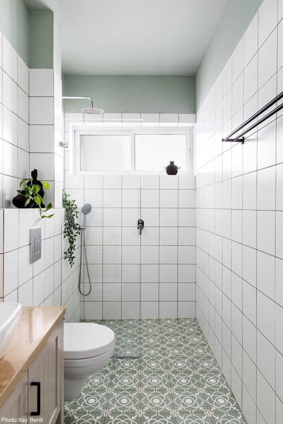a small neutral bathroom with white square tiles, a green and white tile floor, a window, neutral appliances and black touches