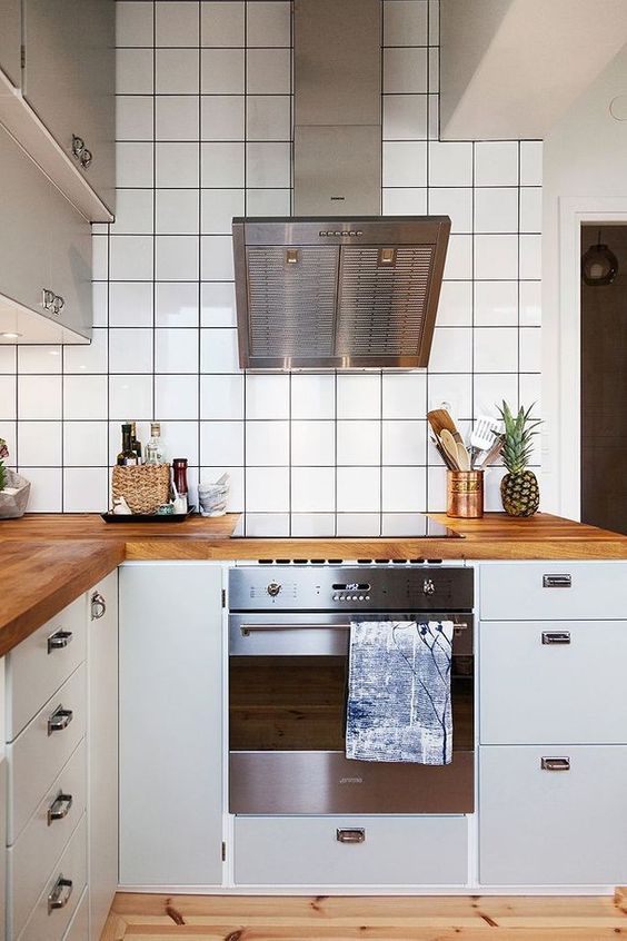 a Scandinavian kitchen with white cabinets, white square tiles on the walls, butcherblock countertops and stainless steel appliances